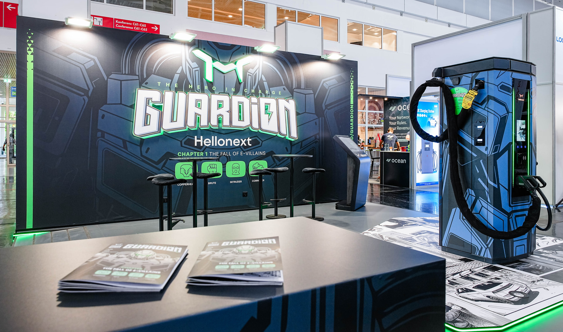 Hellonext GUARDiON booth at Power2Drive Europe: The Fall of E-Villains backdrop, comic books and charger on comic floor graphics
